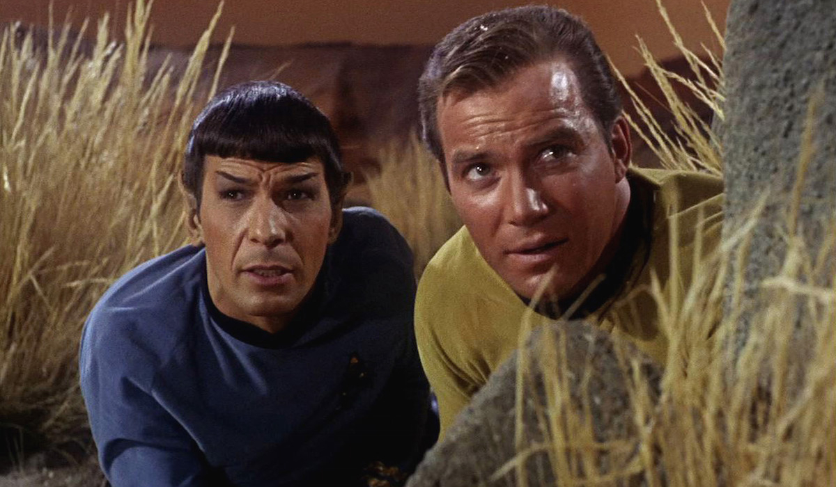 Spock (Leonard Nimoy) and Captain Kirk (William Shatner) crouch in tall grass in 'Star Trek: The Original Series'