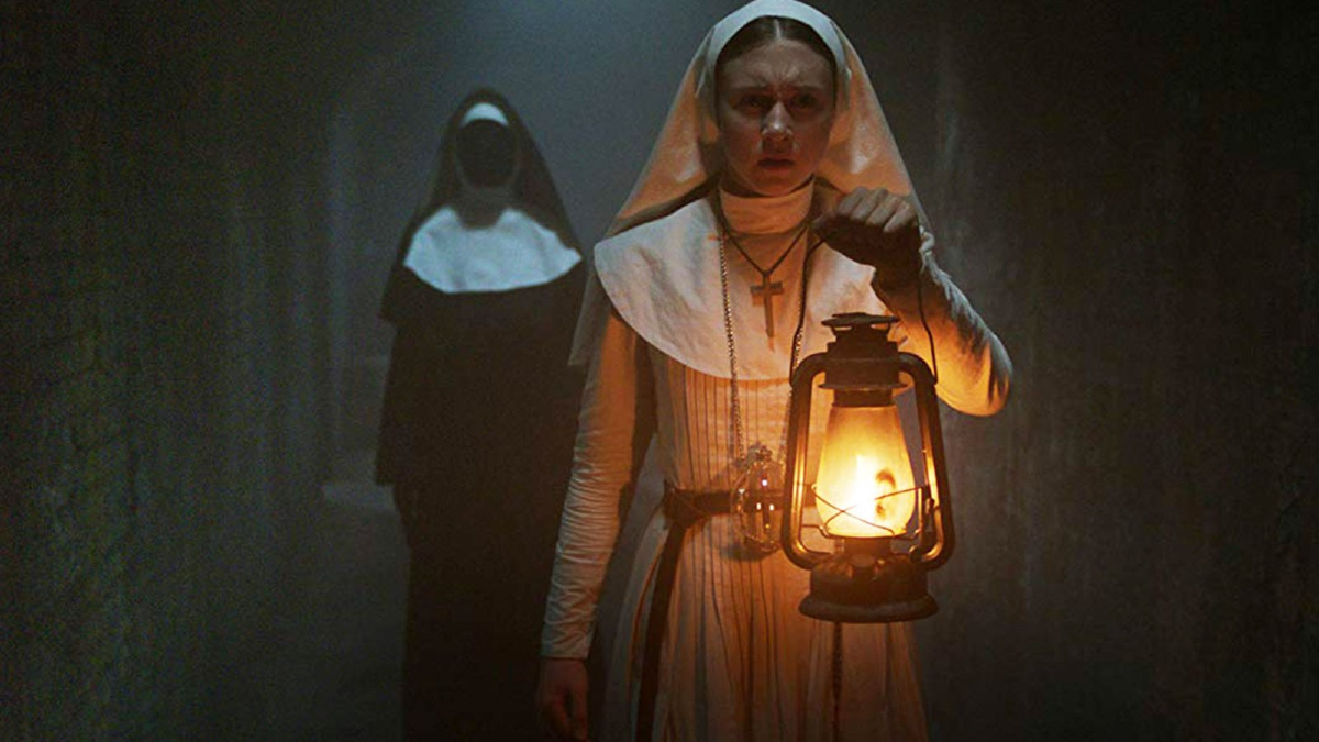 Sister Irene (Taissa Farmiga) lights her way down a dark hall with a lantern while a faceless nun stalks behind her in 'The Nun'