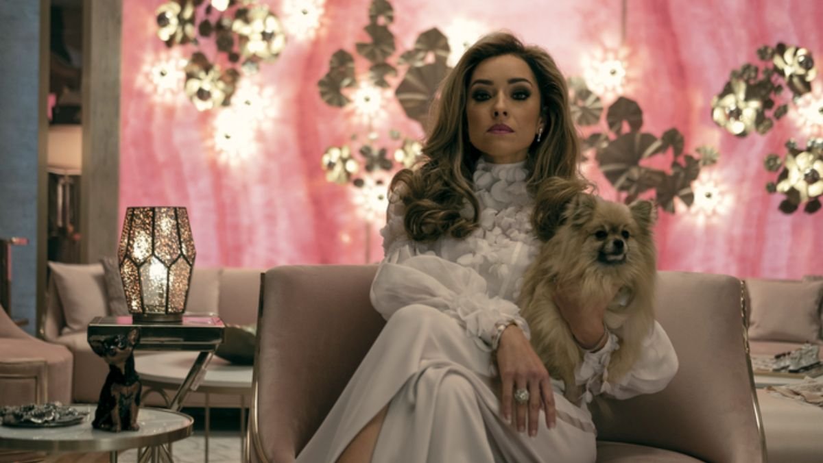 Tatiana sits in a lavishly decorated pink room, wearing a white lacy pantsuit.