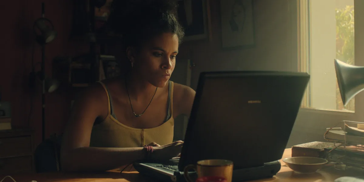 Zazie Beetz frowning while lookikng down at an older laptop in Black Mirror season 6 promo image