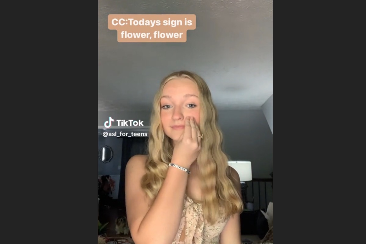 A blonde teenage girl does sign language in a TikTok video.