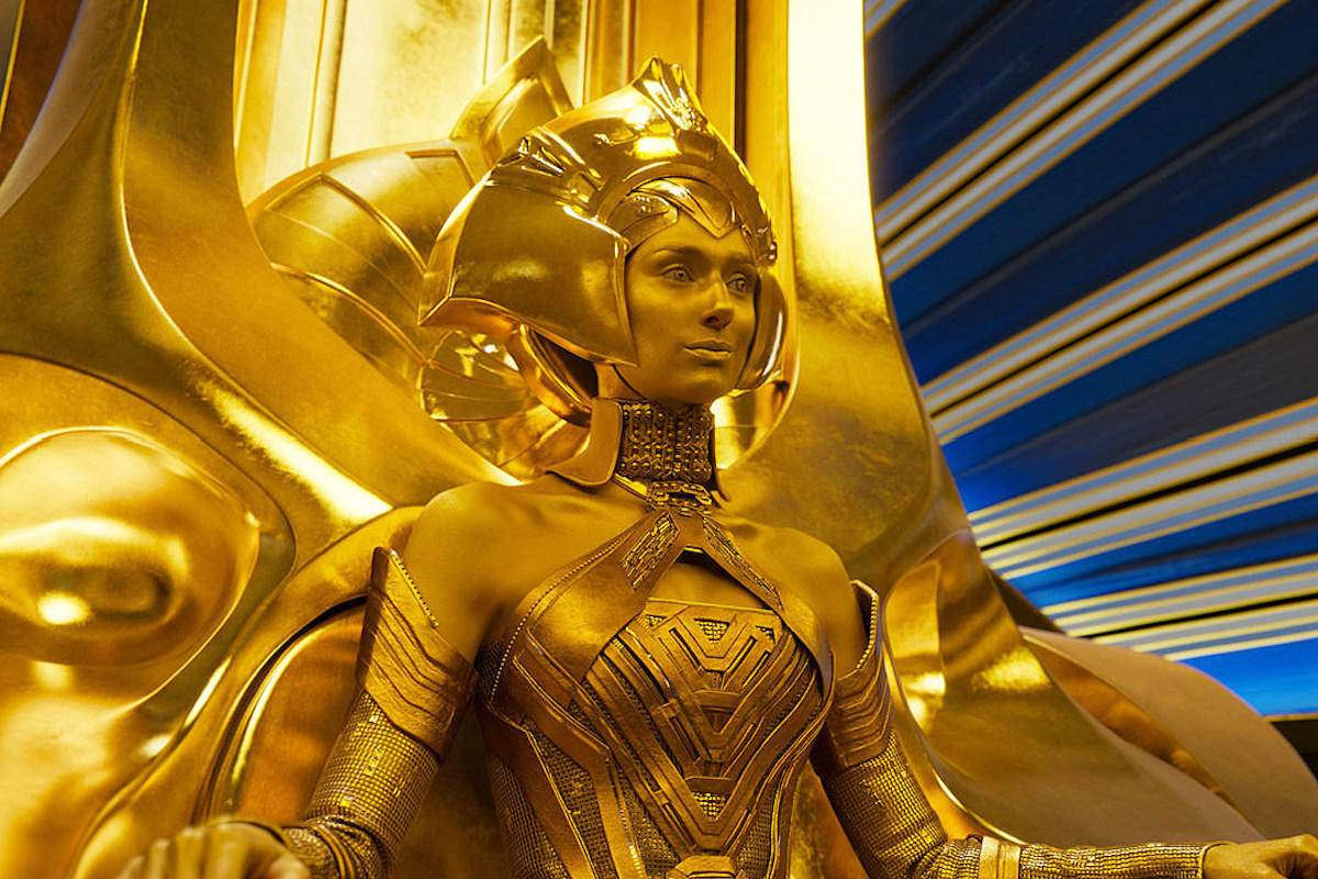 Elizabeth Debicki as Ayesha, a gold woman wearing a golden headdress, sitting in a golden throne.