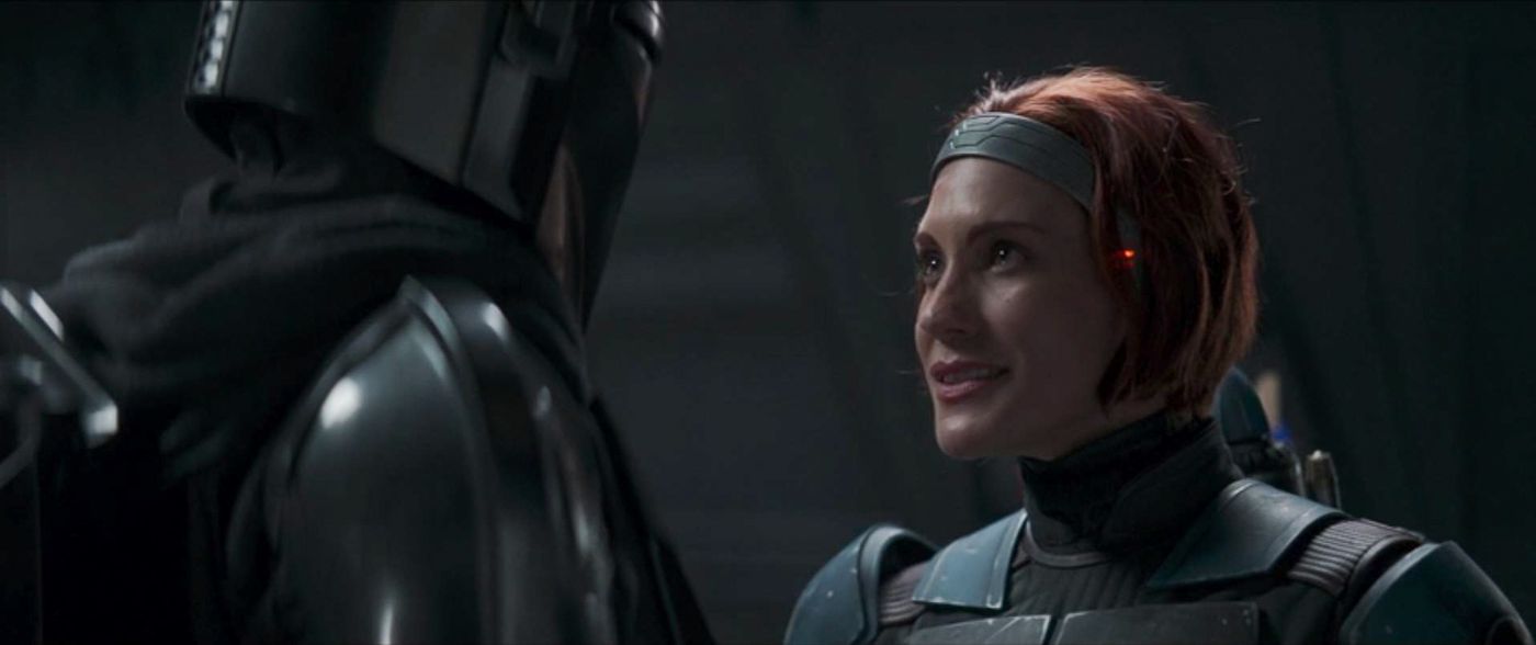 Katee Sackhoff as Bo-Katan Kryze in a scene from 'The Mandalorian' on Disney+. We see her from the shoulders up. She's in her armor, but her helmet's off, so we see her face, grey headband, and chin-length red hair. She's looking up at Din Djarin.