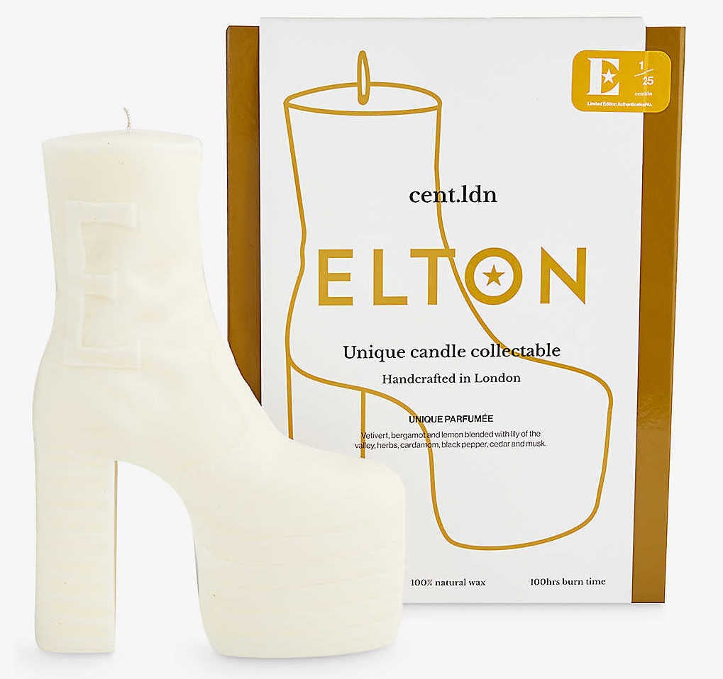 A white candle shaped like a platform boot with a box behind it. The box has a line drawing of the candle on it and Elton in large gold text.