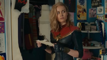 Carol Danvers stands in Kamala Khan's bedroom, holding a torn piece of paper and looking confused.