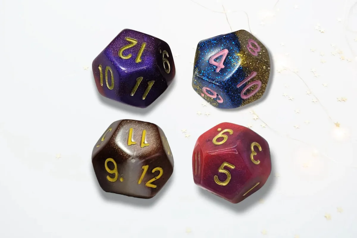 Four 12 sided dice with gold numbers. One red, one purple, one blue and gold, one black and gold.