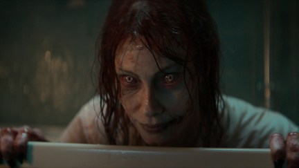 Ellie, in her Deadite form, looks out from the bathtub in Evil Dead Rise. Her eyes have white, demonic-looking irises.