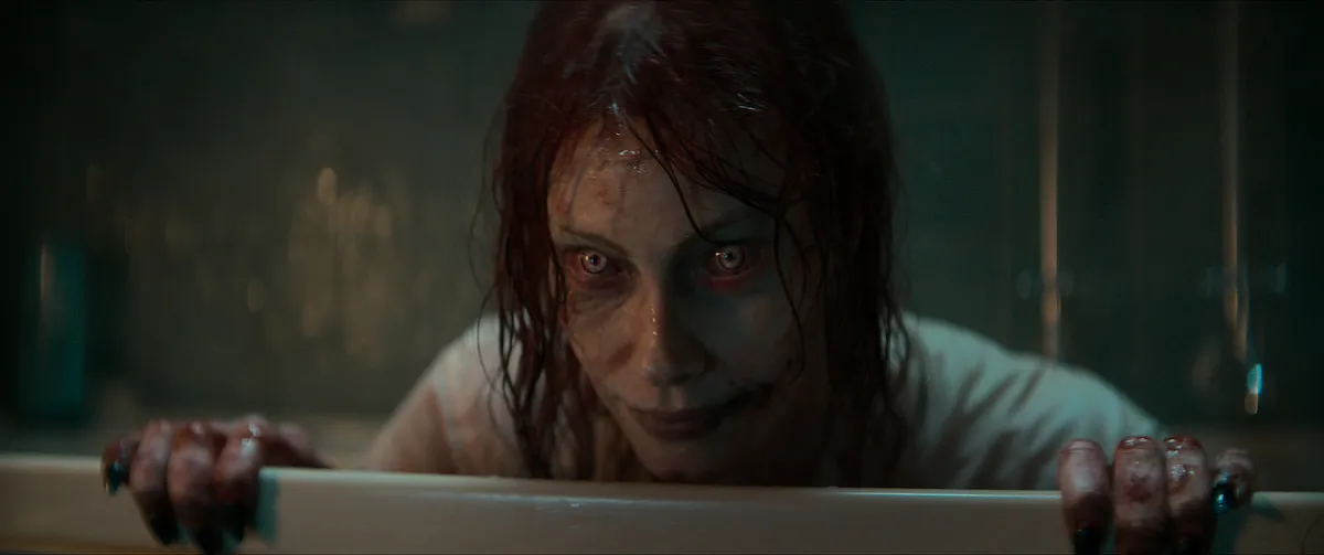 Ellie, in her Deadite form, looks out from the bathtub in Evil Dead Rise. Her eyes have white, demonic-looking irises.