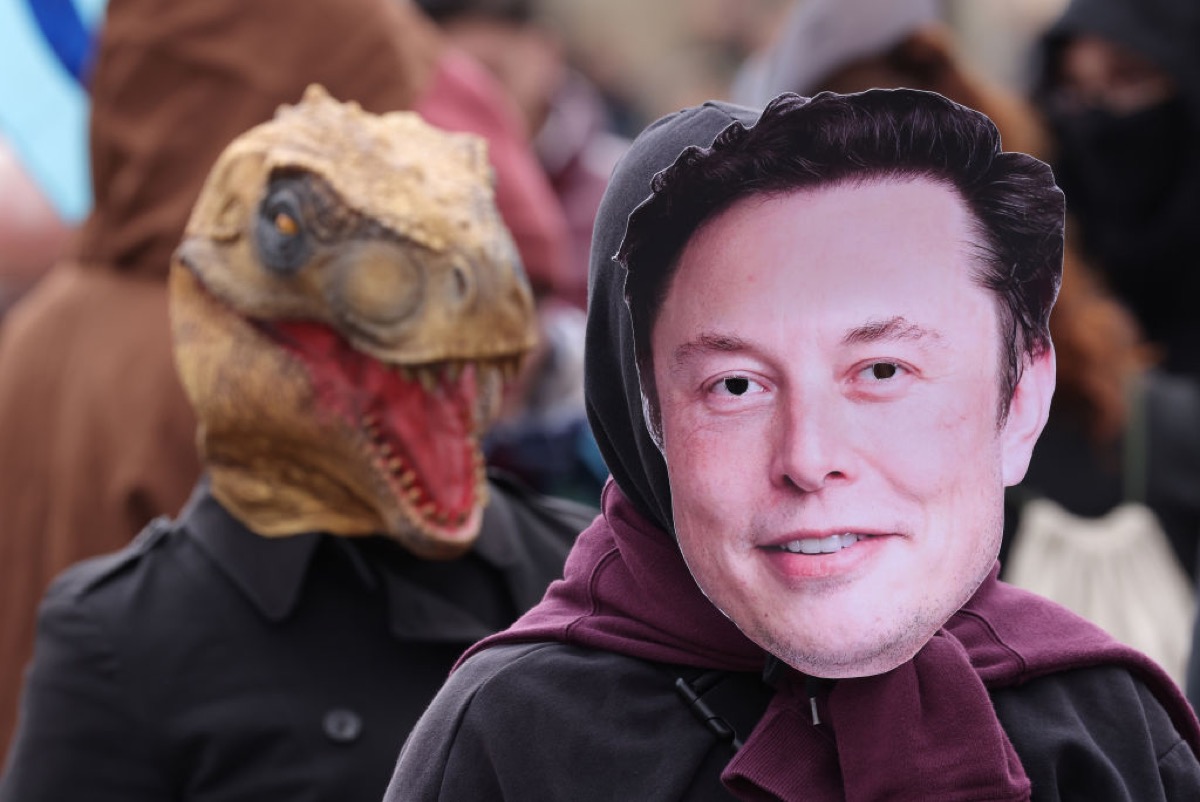 An activist dressed as Elon Musk is trailed by a fellow activist dressed as a fossil fuel lobby dinosaur during a demonstration by the environmental action and human rights group Extinction Rebellion.