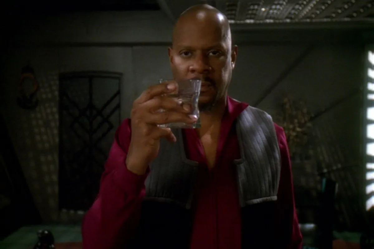 Captain Sisko in Deep Space 9: A shaven headed Black men with a serious expression raises a glass toward the camera.