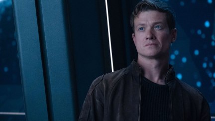 Jack Crusher stands against a window in a spaceship, looking concerned.