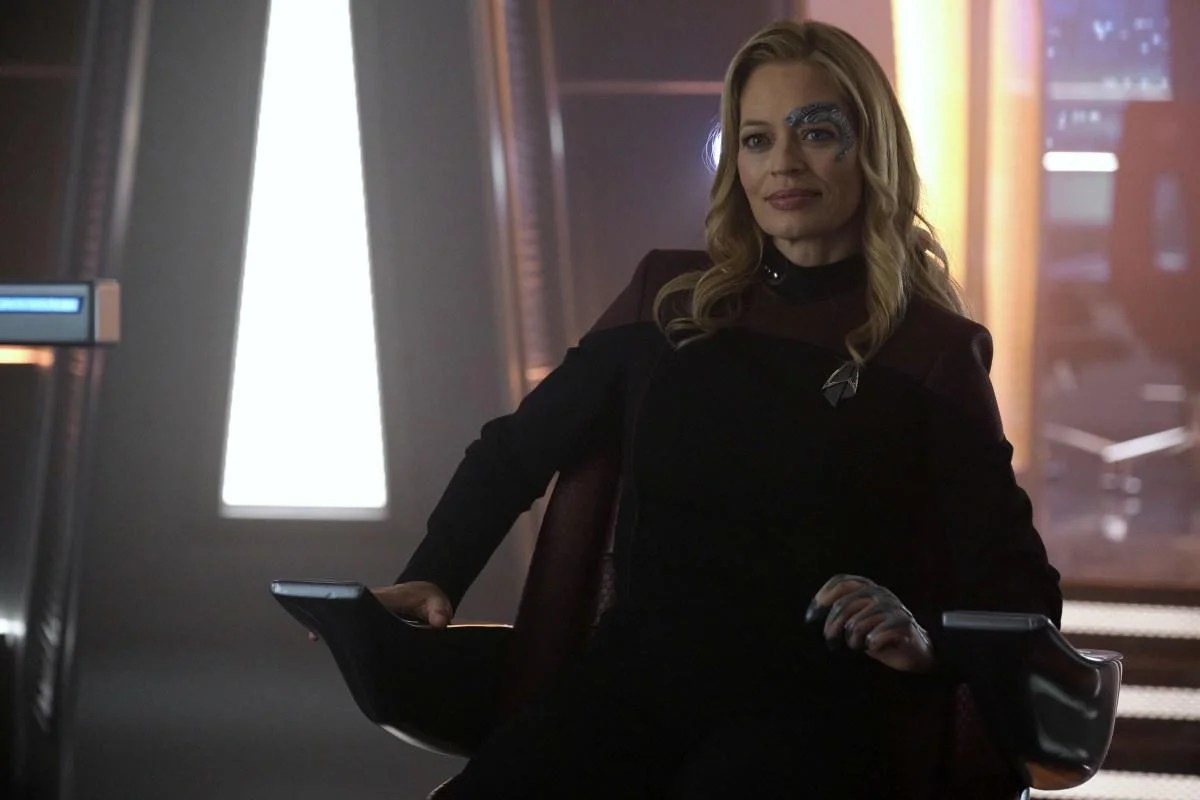 Jeri Ryan as Seven of Nine on 'Star Trek: Picard.' She is a white woman with long blonde hair and wearing a red Starfleet uniform. She has Borg cybernetics around her eye. She's sitting in a captain's chair on a ship. 