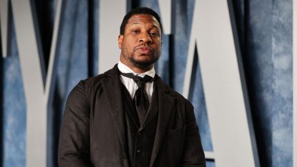 Jonathan Majors looks at the camera, wearing a black suit and tie.