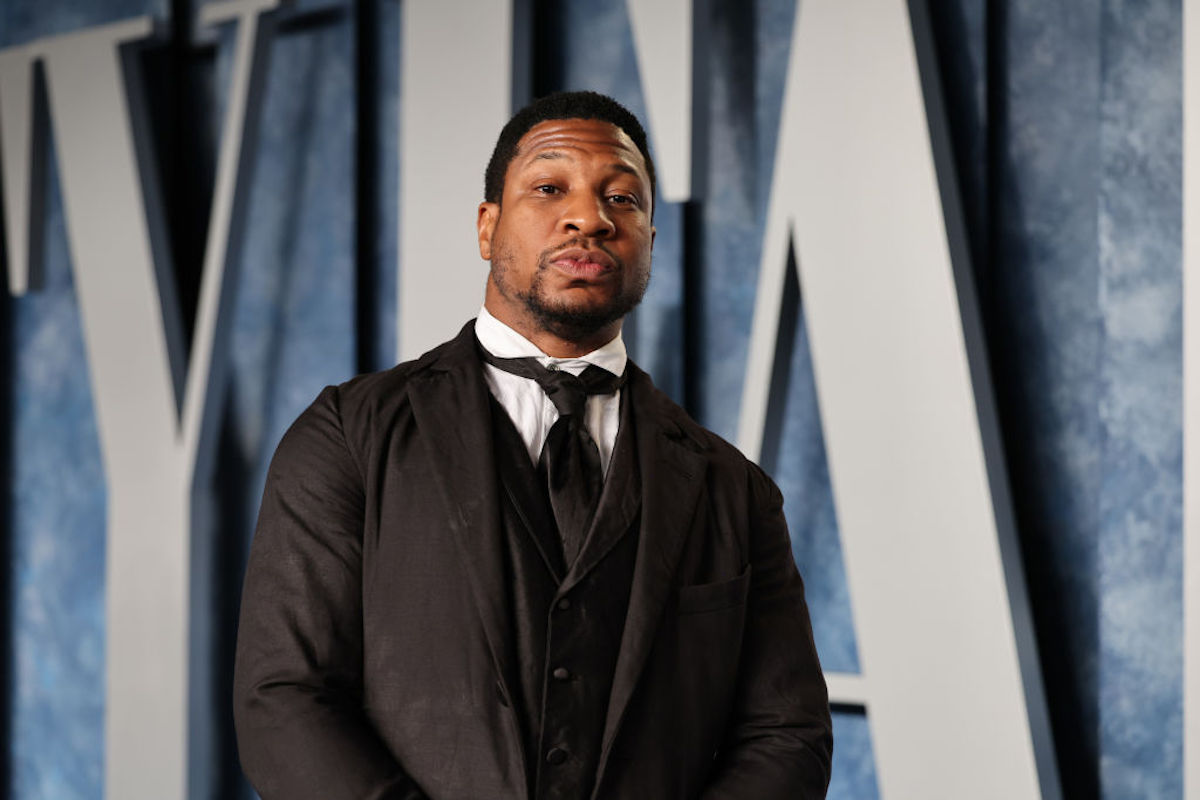 Jonathan Majors looks at the camera, wearing a black suit and tie.