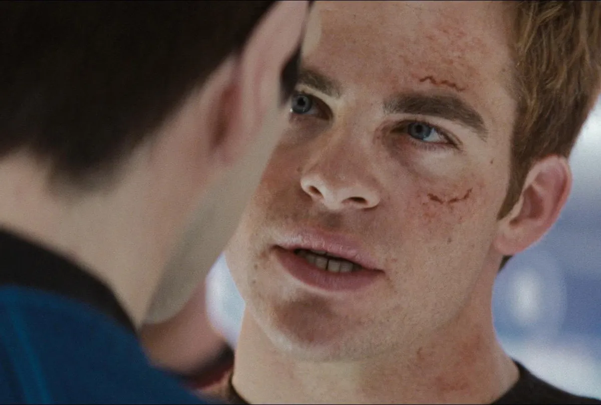 Chris Pine as Captain Kirk in the 2009 'Star Trek' film: A young white man with cuts and bruises on his face stares intently into a dark haired man's face.