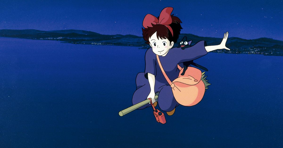 Kiki rides on a broom at night, holding her arm out.
