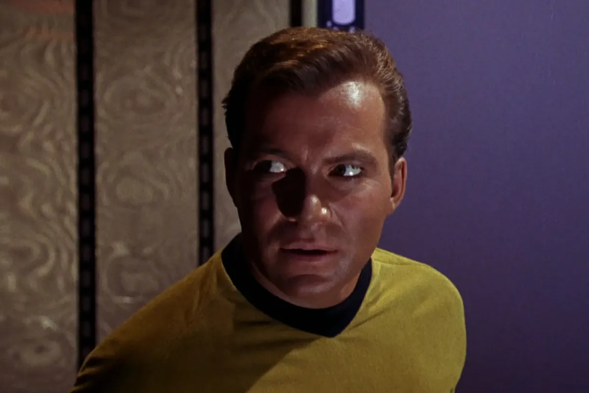 William Shatner as James T. Kirk in 'Star Trek,' the original series: A white man with blonde hair in a yellow Star Trek uniform glances to the side with alarm