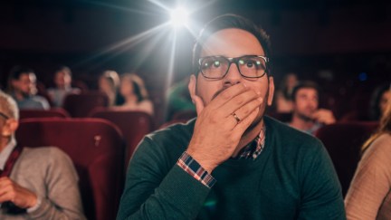 Young man watching a horror movie at the cinema, looking disturbed.