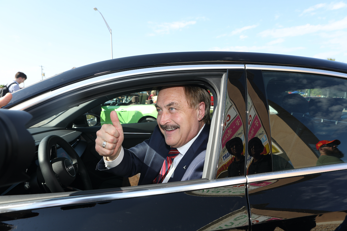 Mike Lindell gives a thumbs up while driving a car.