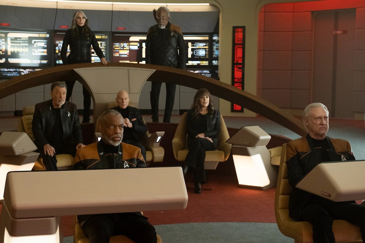 (clockwise l-r): Levar Burton as LaForge, Jonathan Frakes as Riker, Gates McFadden as Crusher, Patrick Stewart as Picard, MichaeL Dorn as Worf, Marina Sirtis as Troi, and Brent Spiner as Data in a scene from the series finale of 'Star Trek: Picard' on Paramount Plus. They are all standing or sitting at their stations on the bridge of the newly refurbished Enterprise-D. Everyone is white except for LaForge and Worf, who are Black men. Crusher and Troi are white women. Worf is a Klingon with a ridged forehead. Data is an android with white hair and yellowish-white skin. Everyone is wearing all black except for LaForge, Worf, and Data, who are wearing gold Starfleet uniforms.