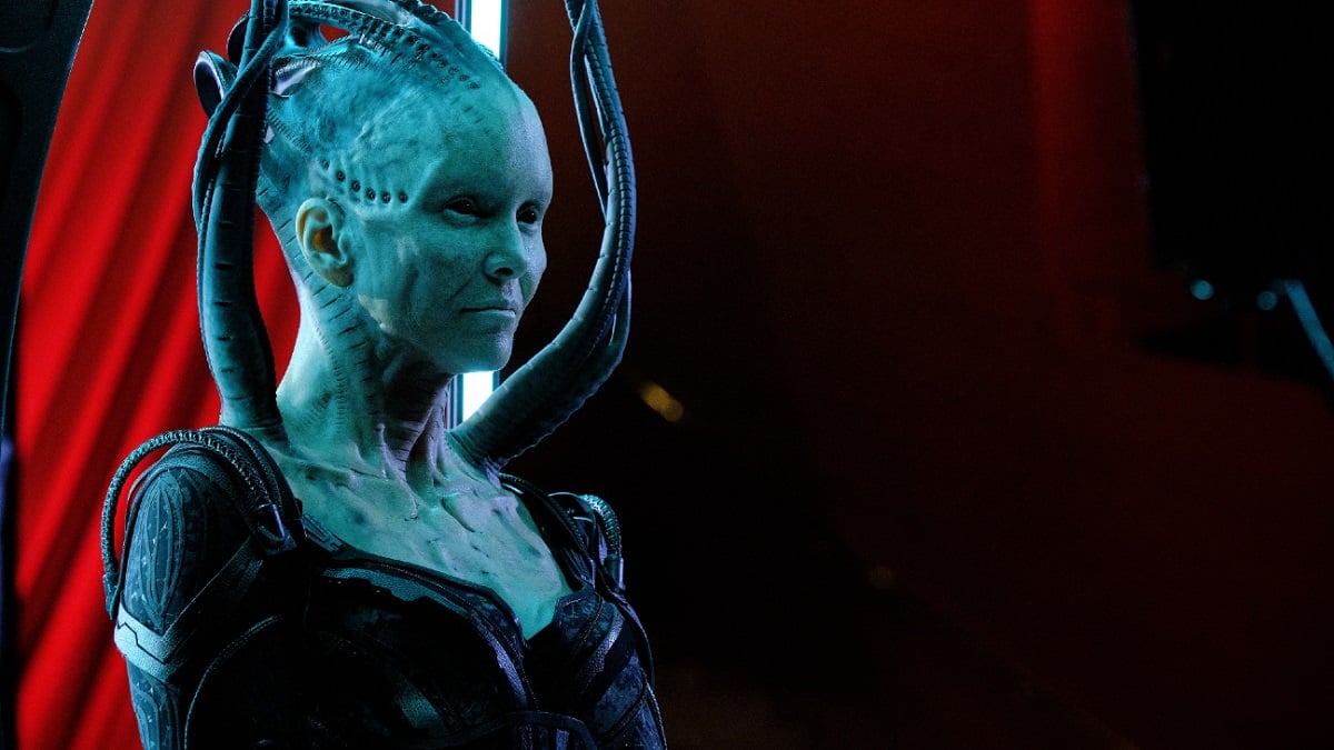 Annie Wersching as the Borg Queen on 'Star Trek: Picard.' She is hanging from her Borg cables at an angle under bluish light. We see her from the chest up. The background is red.