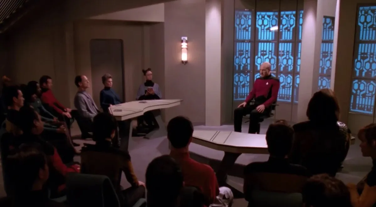 Picard sits on the stand, surrounded by a crowd, in The Drumhead.
