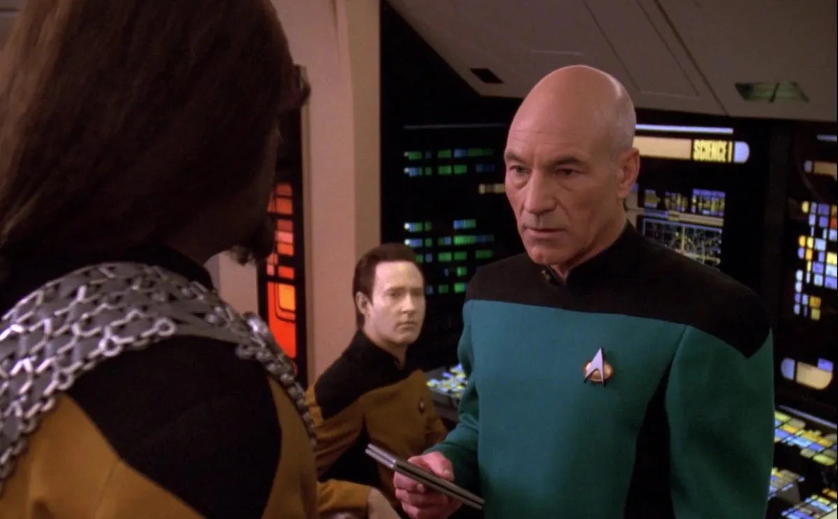 Picard wears a science officer's uniform while talking to Worf.