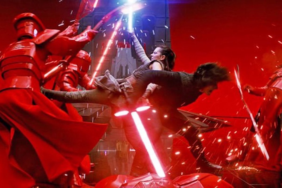 Adam Driver as Kylo Ren, dressed in black flips Daisy Ridley as Rey on his back so she can kick the red armoured praetorian guards. All have red lightsabers except Rey, whose lightsaber is blue.