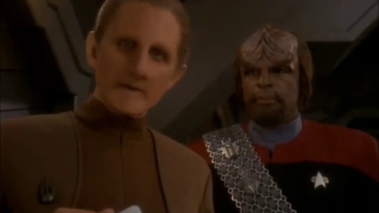 Rene Auberjonois as Odo and Michael Dorn as Worf on 'Star Trek: Deep Space Nine.'  Odo is a white Changeling who's adopted a male humanoid shape with blond, slicked back hair and wearing a brown Starfleet uniform. He's looking into the distance at something. Worf is a Black Klingon with thick ridges on his forehead, brown hair, and he's wearing a red Starfleet uniform with a silver Klingon warrior sash over it. He stands behind Odo looking at him.