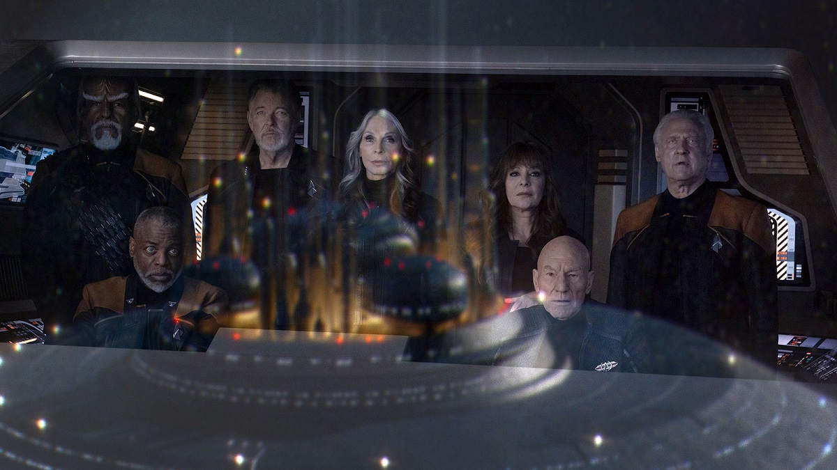 (l-r) Michael Dorn as Worf, LeVar Burton as LeForge, Jonathan Frakes as Riker, Gates McFadden as Dr. Crusher, Marina Sirtis as Troi, Patrick Stewart as Picard, and Brent Spiner as Data in a scene from 'Star Trek: Picard" on Paramount plus. They are standing together on a shuttle bridge looking out the window at the Federation museum, which is reflected in the glass.
