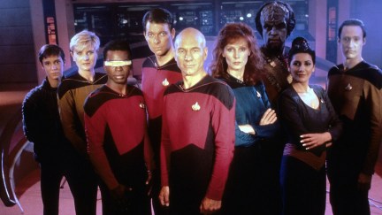 The cast of Star Trek: The Next Generation poses with computer panels in the background.