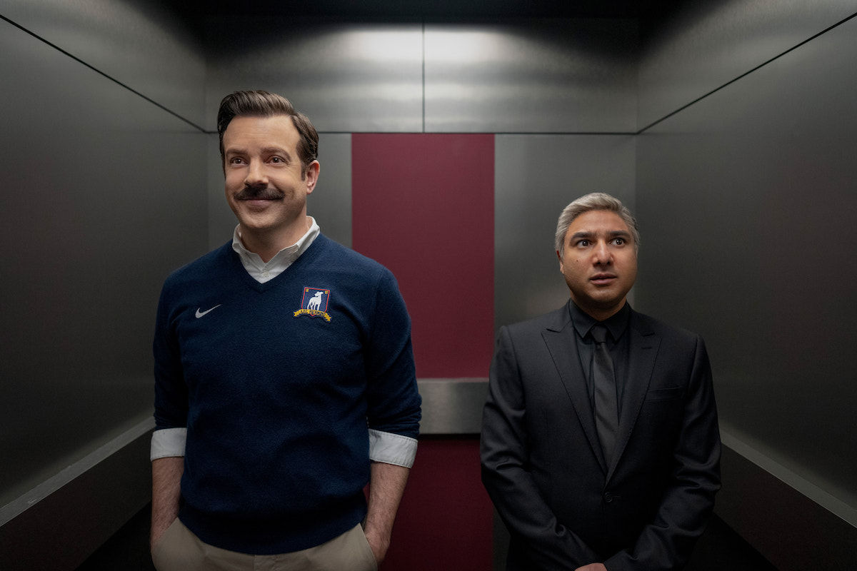 Ted and Nate stand in an elevator together. Ted is smiling, but Nate looks pensive.