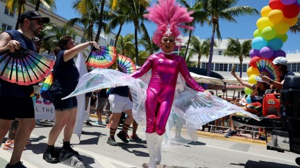 A performer in a bright pink body suit dances at a Pride parade
