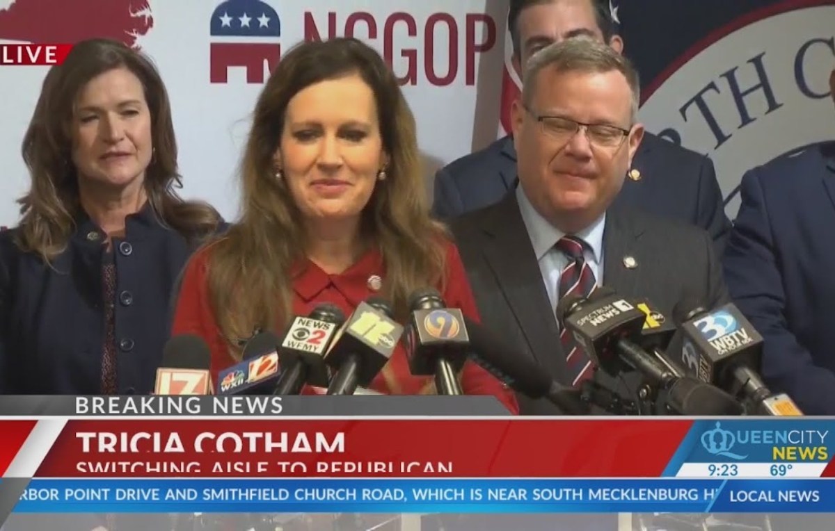 A white woman (Tricia Cotham) speaks into a group of microphones at a news conference.