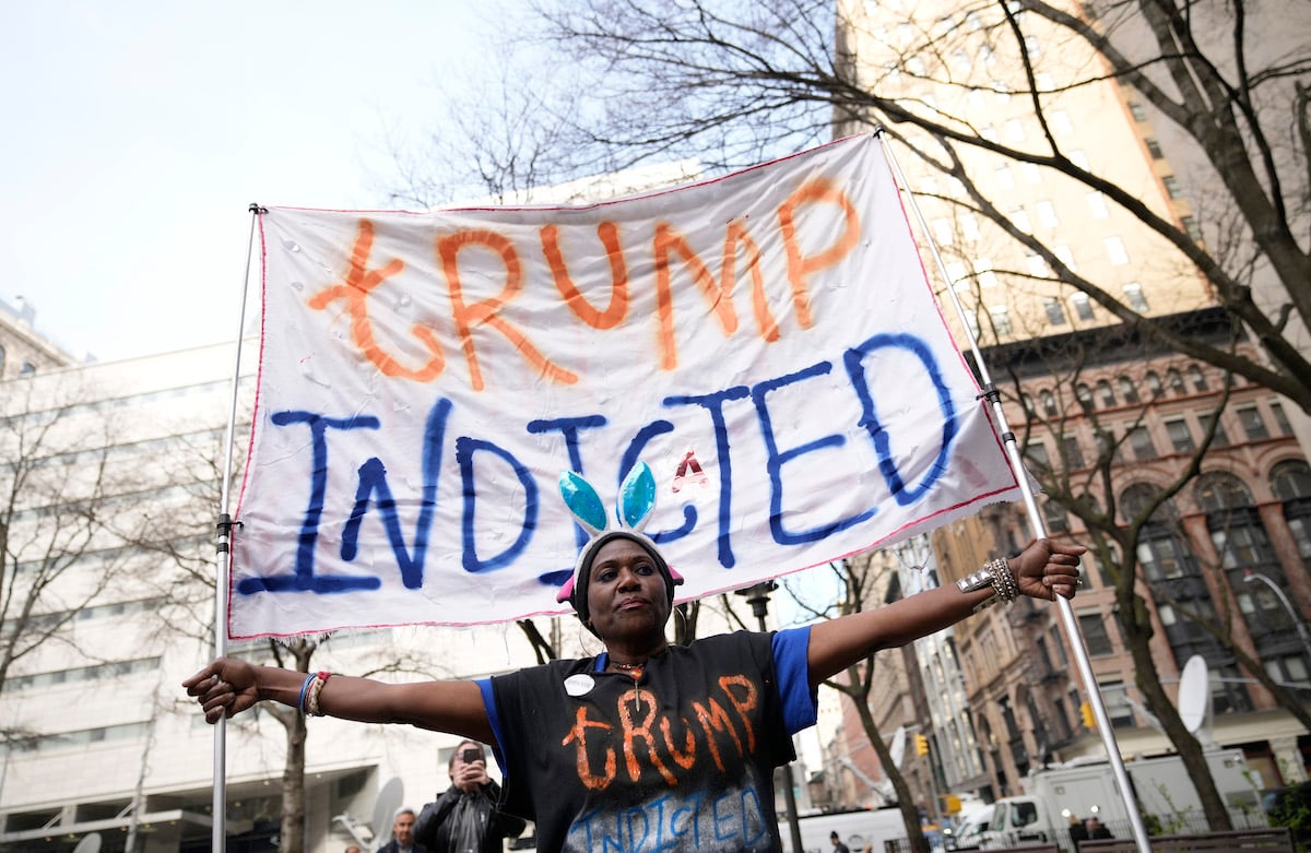 A Black woman holds a giant banner reading "Trump indicted"