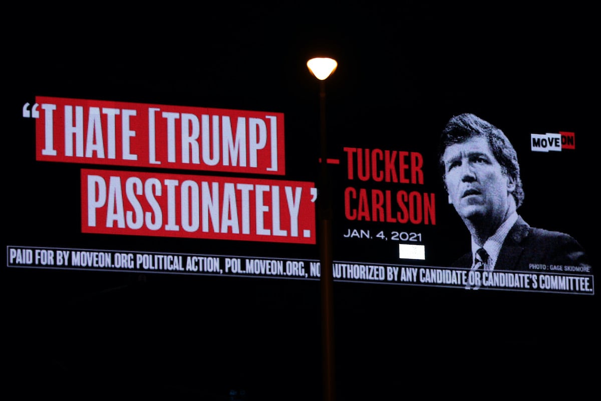 A digital billboard featuring Tucker Carlson's face and a large caption reading "I hate [Trump] passionately."