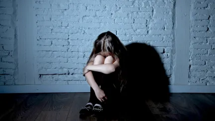 A young girl, sitting on the floor, with her knees pulled up to hide her crying face.