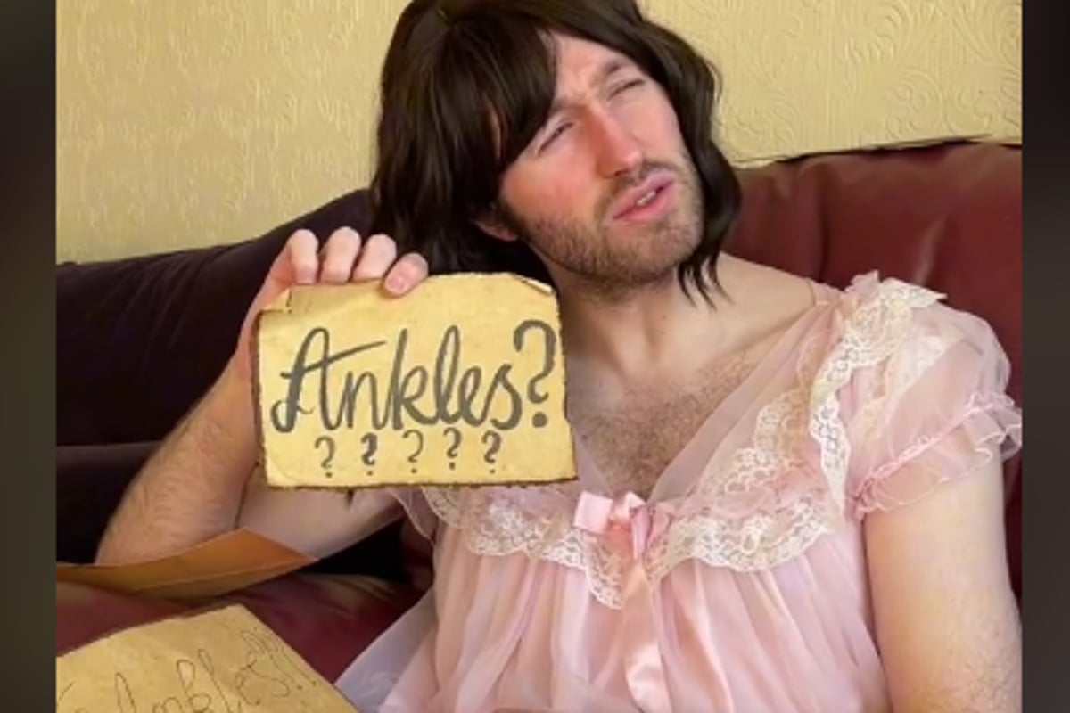 Christian Brighty, wearing a brown wig and a pink nightgown, holds up a brow paper missive with "ankles?" written on it over a line of question marks. He is making a sarcastic face.