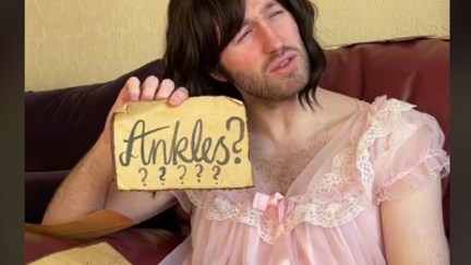 Christian Brighty, wearing a brown wig and a pink nightgown, holds up a brow paper missive with 