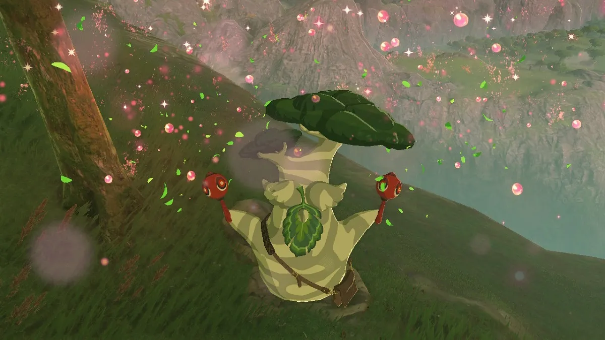 Screenshot of Hestu from 'The Legend of Zelda: Breath of the Wild." Hestu, a Korok, is a chubby being with a dark and light green camouflage-printed body and a tree for a head. He has a large leaf for a face and a brown messenger bag across his body. He is holding out a pair of red maracas in a celebratory fashion as colorful leaves fall down around him like confetti. He's standing at the edge of a hill overlooking a valley. 
