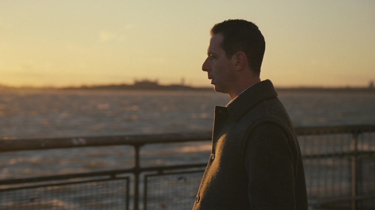 Image of Jeremy Strong as Kendall Roy in a scene from HBO's 'Succession.' It's daylight, and we see Kendall in profile wearing a brown, wool coat overlooking the Hudson River in a state of despair.