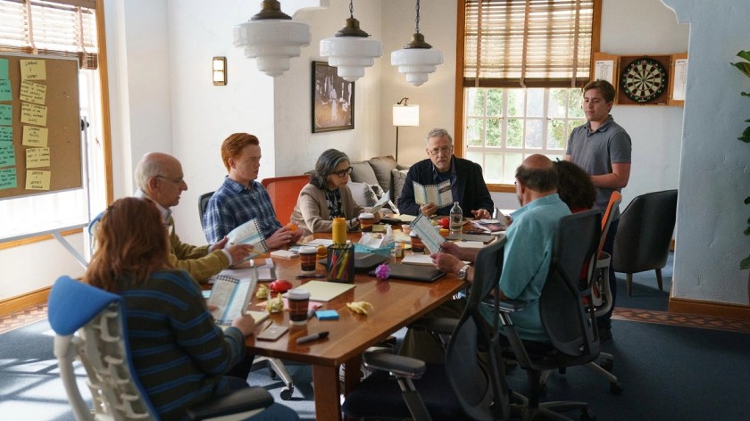 Image of the fictionaI writers' room on Hulu's 'Reboot.' Paul Reiser is at the head of the table surrounded by seven other people sitting around a cluttered conference room table. 