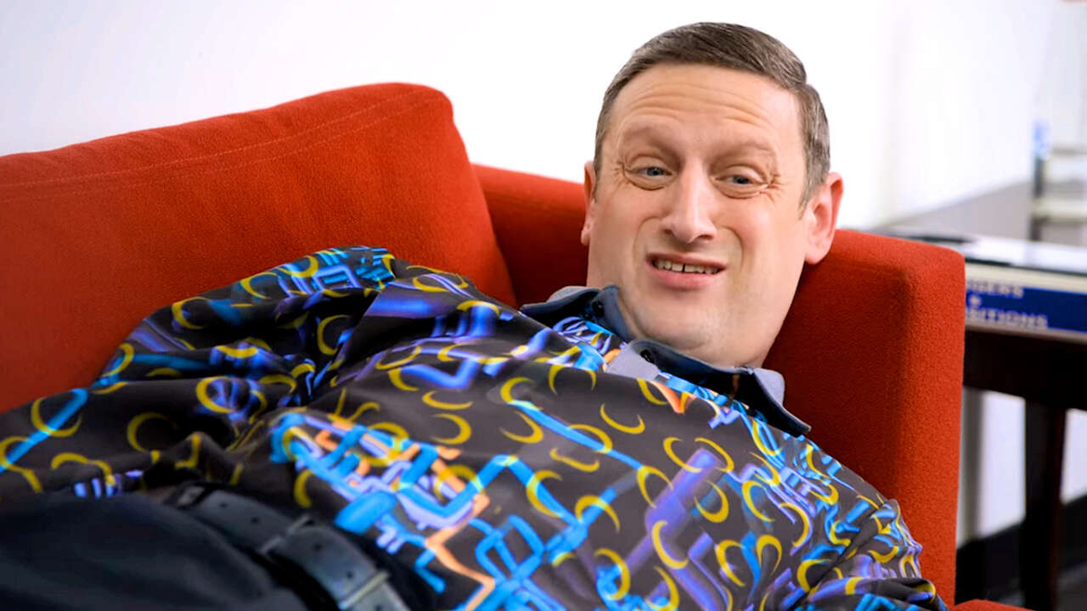 Tim Robinson is lying down on a couch and wearing a shirt with an elaborate pattern in 'I Think You Should Leave.'