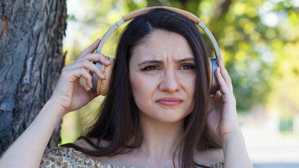 A woman frowns, pulling one side of her headphones away from her ear.