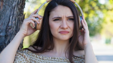 A woman frowns, pulling one side of her headphones away from her ear.