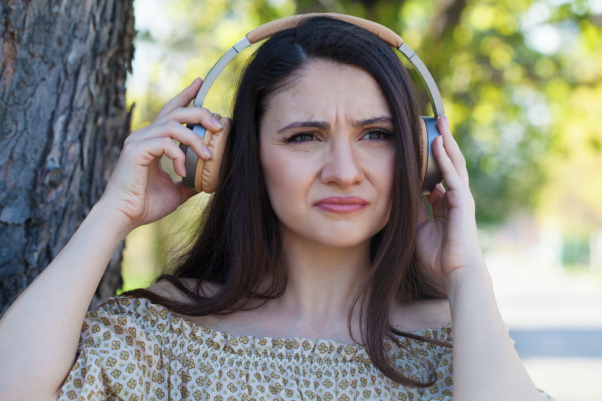 A woman frowns, pulling one side of her headphones away from her ear.