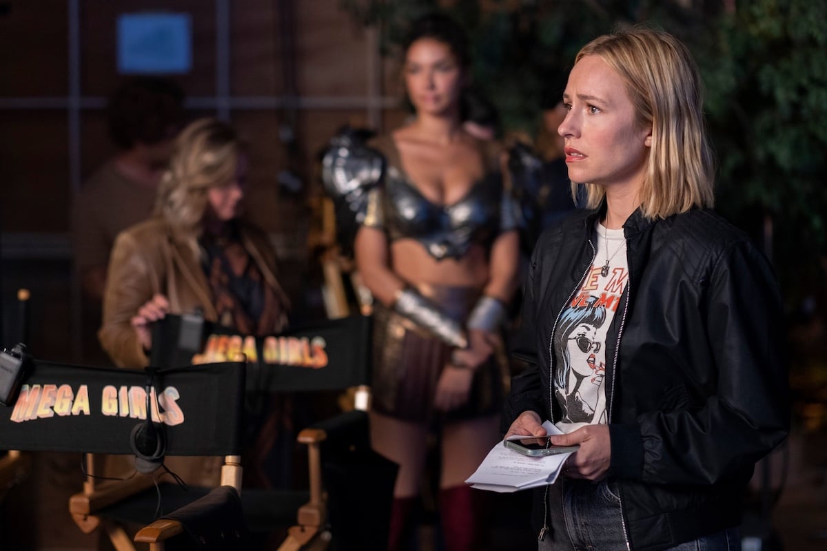 Sally sits in a chair on a movie set, with women in armor standing behind her. "Mega Girls" is written on two empty chairs.
