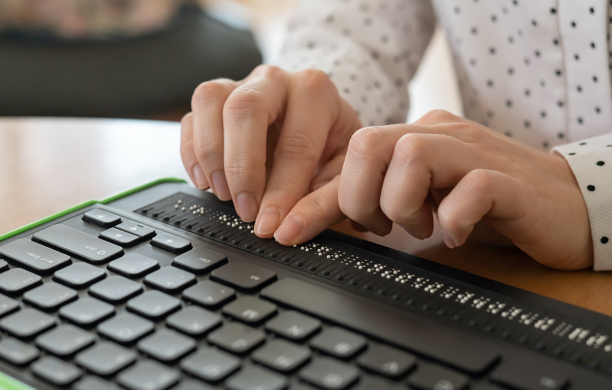 Closeup on a woman's hands using a braille keyboard.