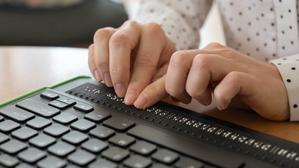 Closeup on a woman's hands using a braille keyboard.