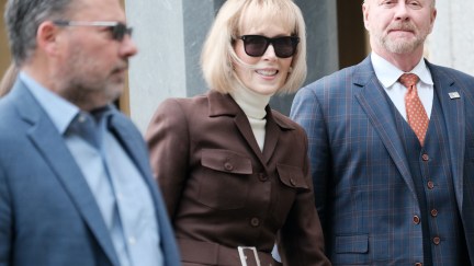 E Jean Carroll leaves a courthouse wearing a turtleneck and coat, flanked by two men.